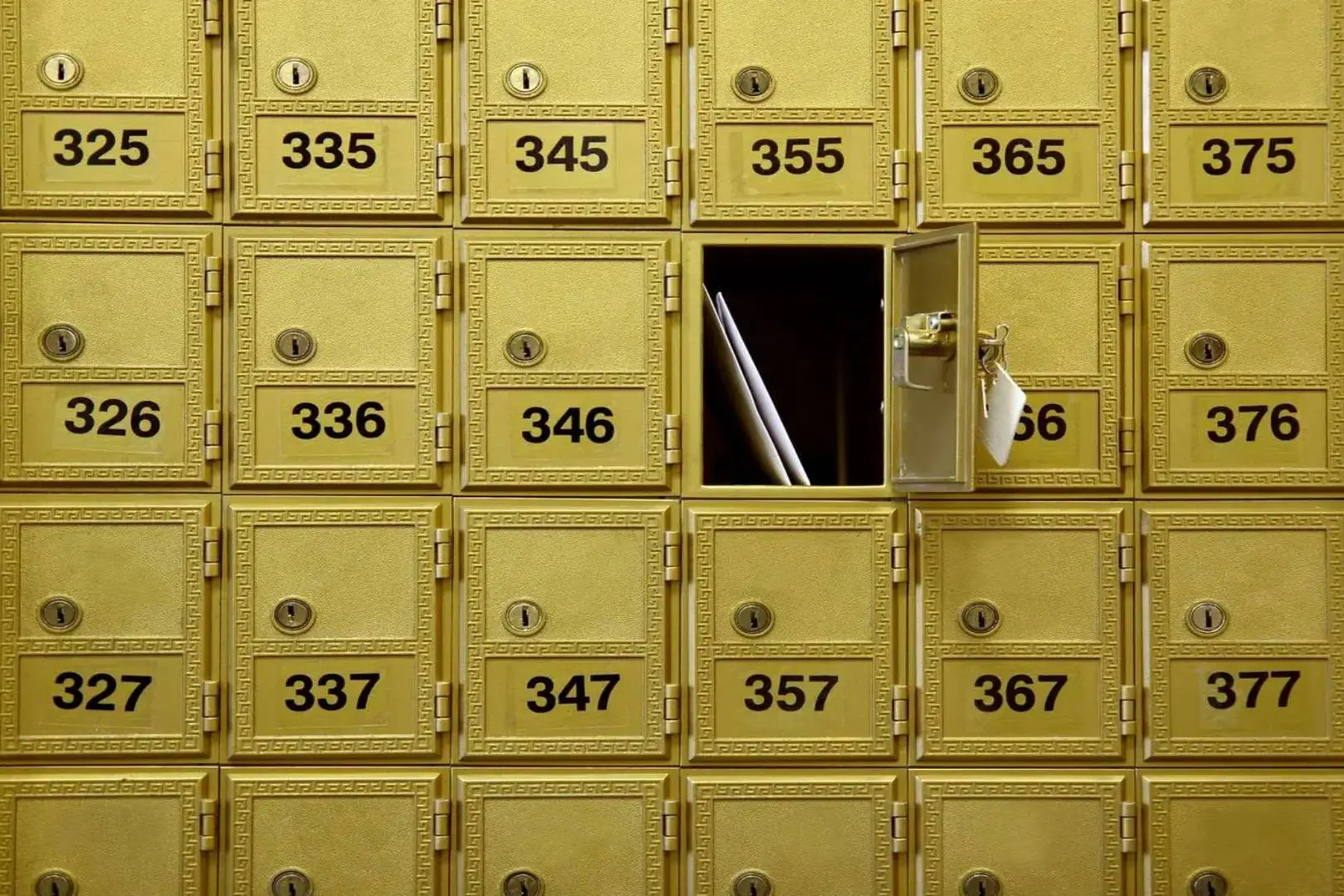 A bunch of yellow mailboxes with one open door.